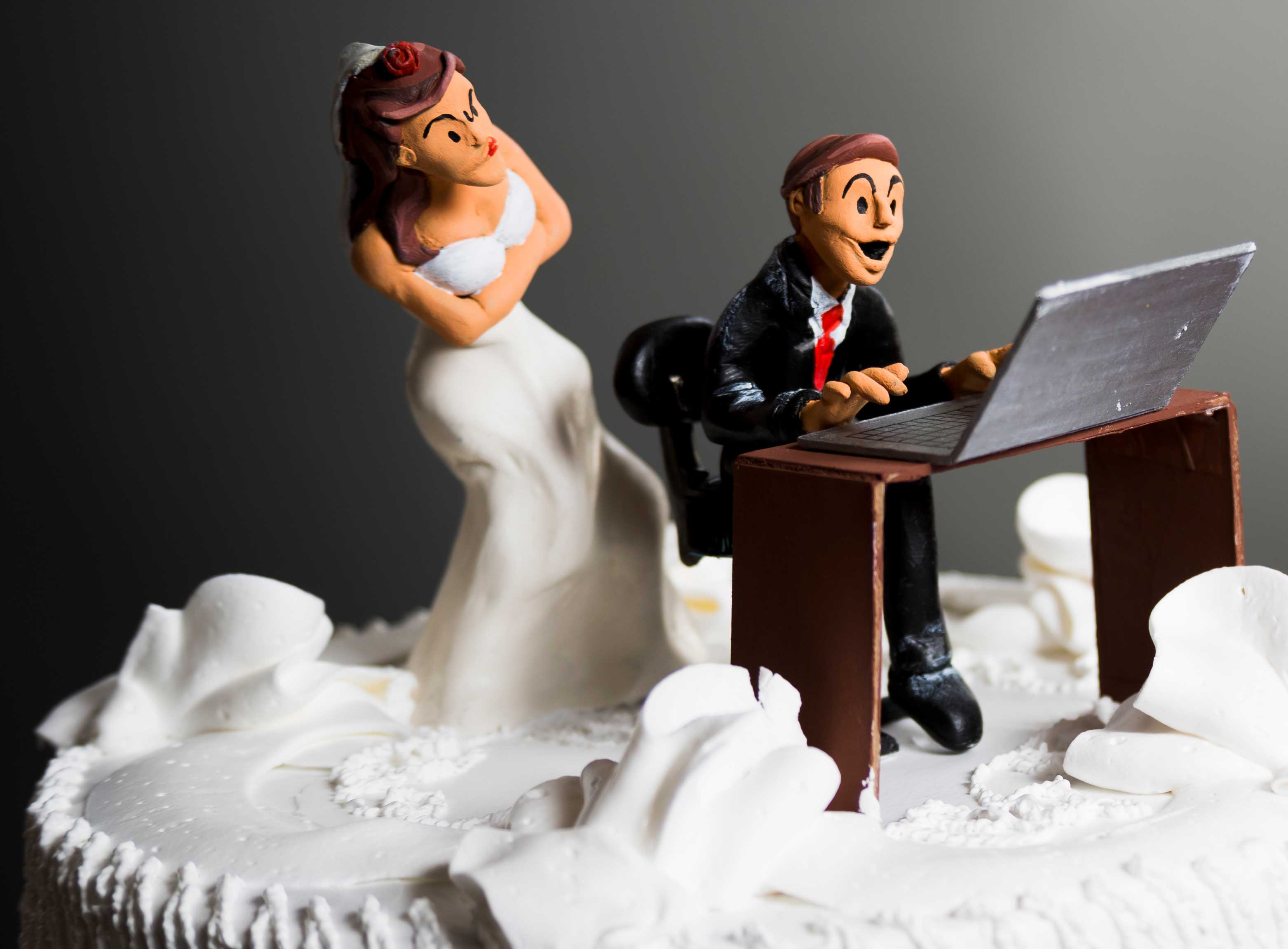 Wedding cake figurines: a bride waits beside a groom seated at a laptop.
